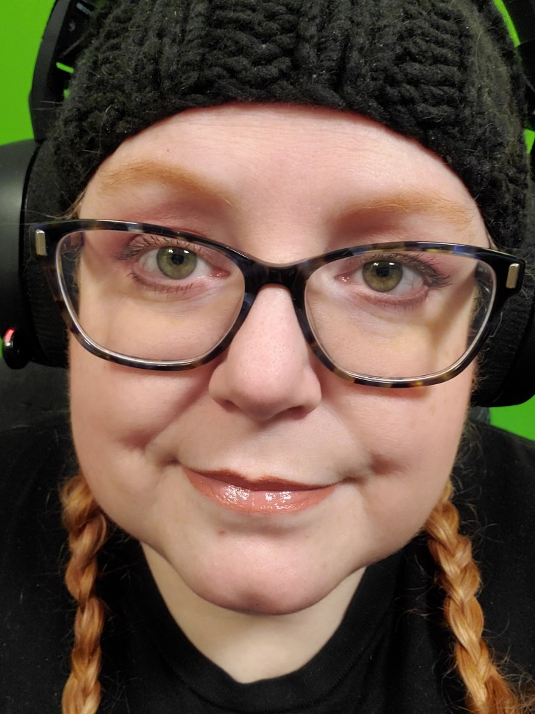 Selfie featuring a red haired woman with curly hair and dark brown glasses named Jenn wearing a black knit hat